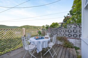 An outdoor patio with a round table and chairs, a white fence, and a view of green hills. - 2 Bed in Looe (oc-v28787) (Looe)