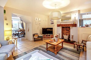 A cozy living room with a fireplace, a television, and a dining area with a table and chairs. - 3 Bed in Appledore (oc-t28375) (Appledore)