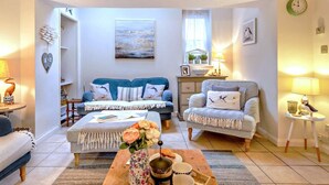 Ein gemütliches Wohnzimmer mit Sofa, Sessel und Couchtisch, mit einem Gemälde, einer Uhr und einer Blumenvase.