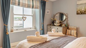 Ein Schlafzimmer mit Bett, Kommode, Spiegel und einem Fenster mit Vorhängen.