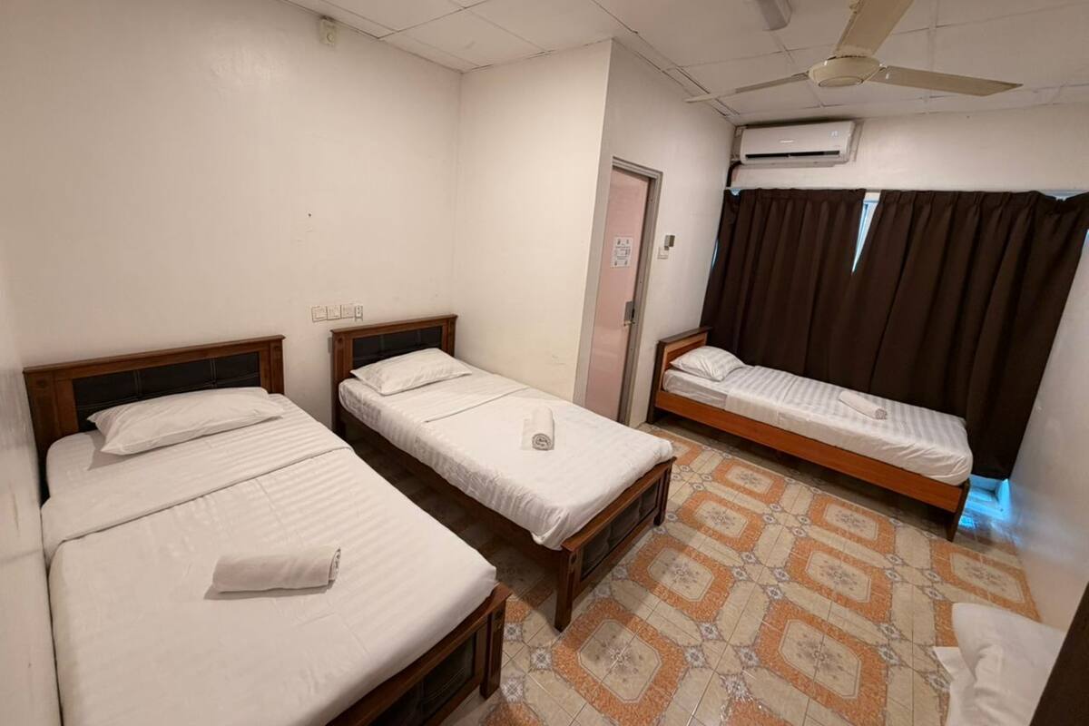 A hotel room with three single beds, a ceiling fan, an air conditioning unit, and a patterned floor.