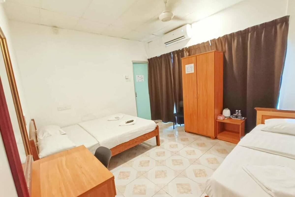 A hotel room with two single beds, a wooden wardrobe, a small table, and a ceiling fan.