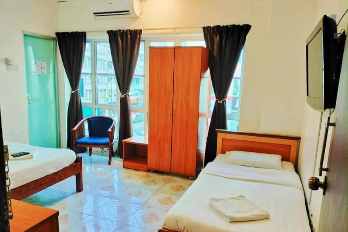 A hotel room with two single beds, a wooden wardrobe, a chair, and a television.