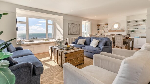 Un salón amplio con vistas al mar, que incluye un sofá azul, sillones blancos y una mesa de centro rústica.
