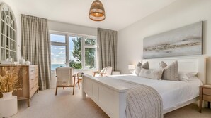 Un dormitorio con una cama grande, un escritorio y una silla, una ventana amplia con cortinas y vistas al exterior.