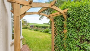 En pergola av trä med ett spaljéliknande mönster, som leder in till en frodig, grön trädgårdsdel.