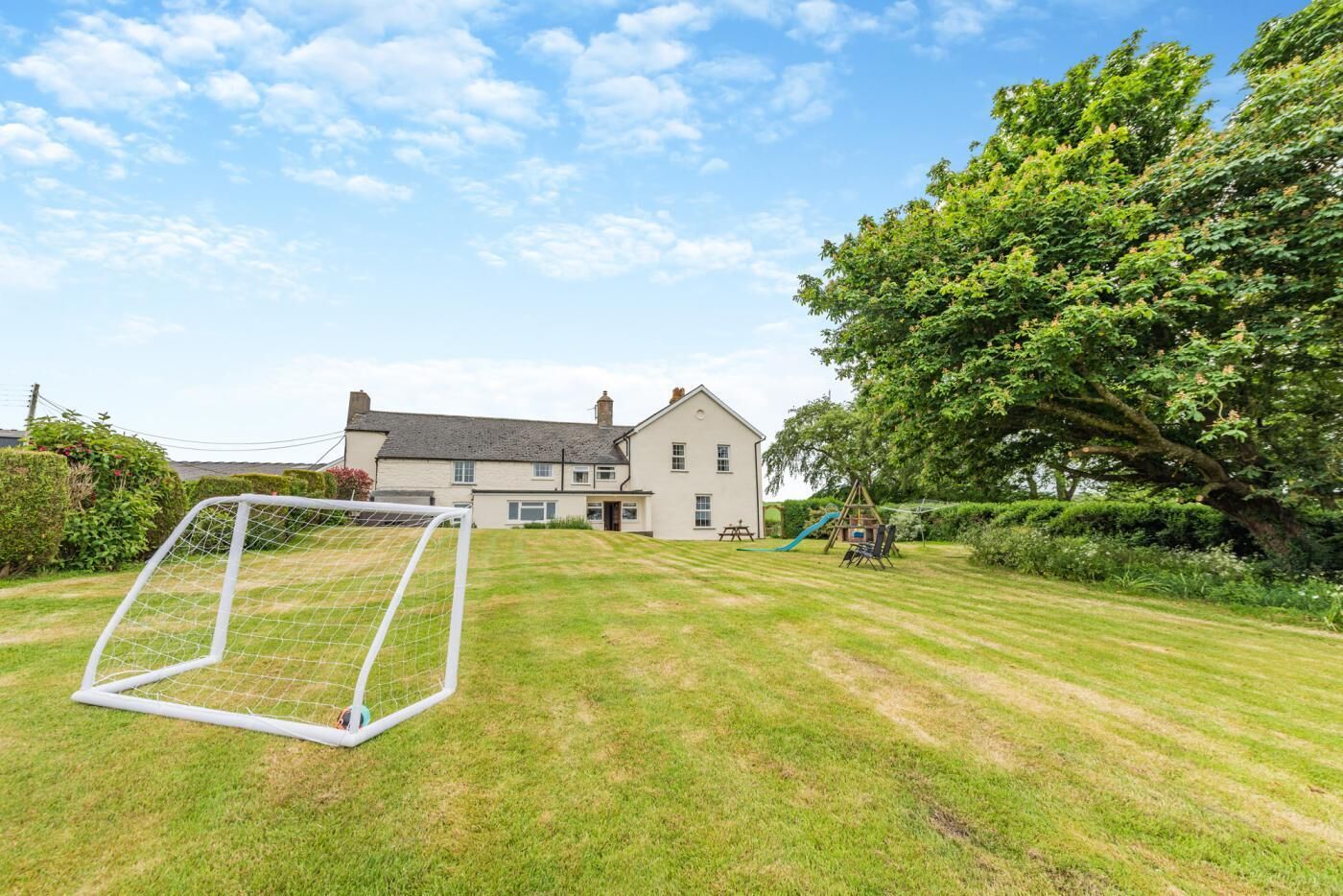 A residential property with a well-maintained lawn, a soccer goal, and a play area with a slide and swings.