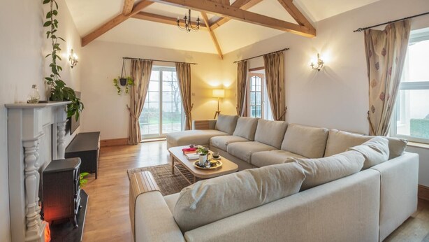 A spacious living room with a large beige sectional sofa, a fireplace, and a wooden ceiling structure. - 5 Bed in Mynytho (oc-c28916) (Mynytho)
