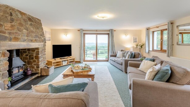 Ein gemütliches Wohnzimmer mit Kamin, Flachbildfernseher, einer Couch und Blick ins Freie.