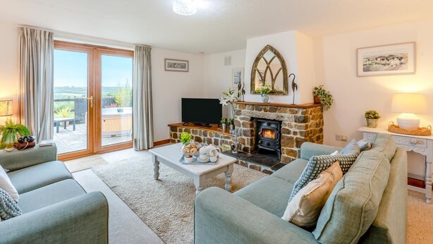 A living room with a stone fireplace, a television, and a balcony with curtains. - 3 Bed in East Chilla (oc-t28939) (Black Torrington)