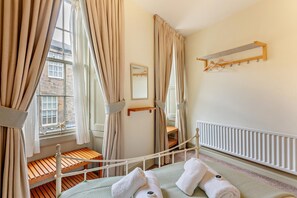Een slaapkamer met een bed, een houten bankje, een radiator en een raam met gordijnen.