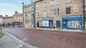 A street with a cobblestone path, a pedestrian crossing, and a building with a blue storefront labeled "PENN GALLERY". - 2 Bed in Alnwick (oc-f28915) (Alnwick)