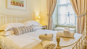 A neatly made bed with white linens and a striped pillow, a bedside lamp, and a window with curtains. - 2 Bed in Alnwick (oc-f28915) (Alnwick)