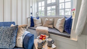 En mysig sittplats med en bänk och kuddar, en skål med frukt och två muggar på ett bord.