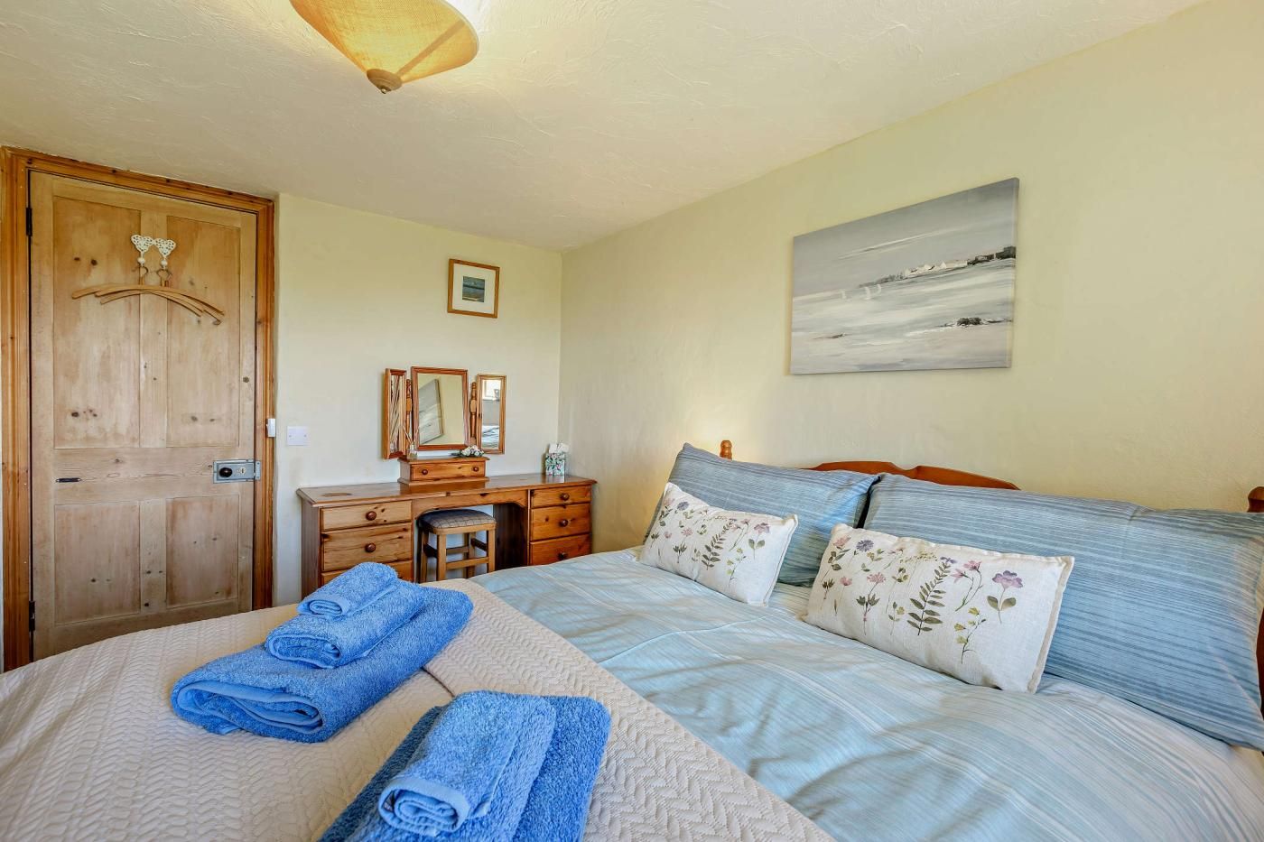 Una camera da letto con un letto, una cassettiera in legno, uno specchio e un quadro appeso al muro.