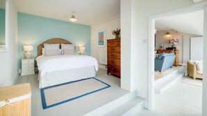 Een slaapkamer met een bed, nachtkastjes, een kaptafel en uitzicht op een aangrenzende woonruimte.