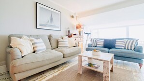 Een woonkamer met twee banken, een bijzettafeltje, een lamp en een lijst met een afbeelding aan de muur.
