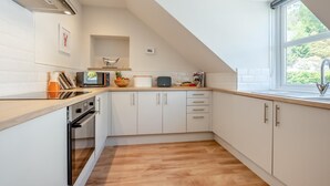 A modern kitchen with white cabinets, a wooden countertop, a built-in oven, and a window providing a view of greenery outside. - 1 Bed in Looe (oc-s29019) (Looe)