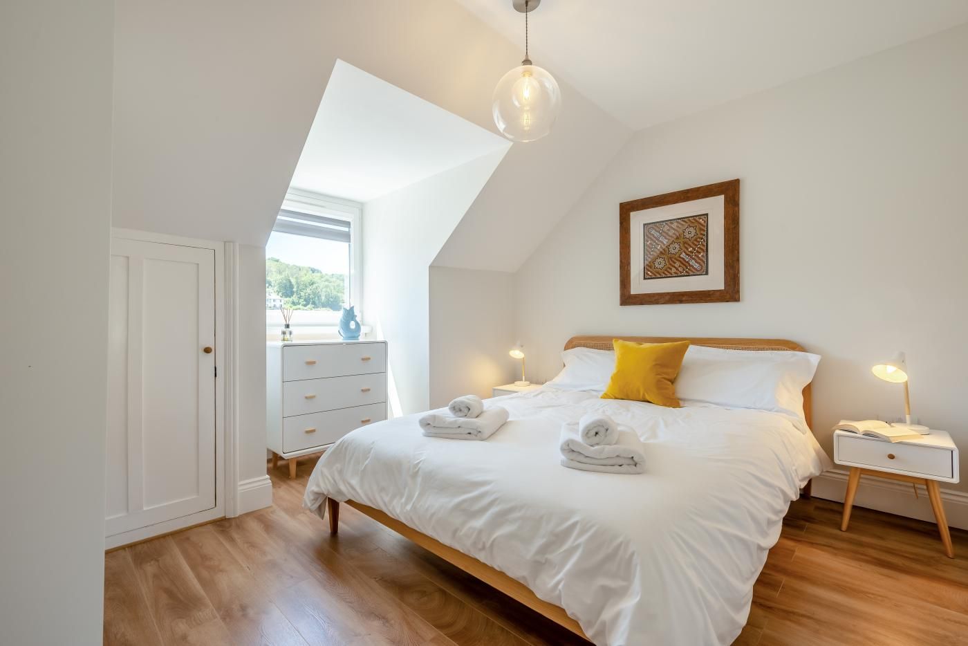 A bedroom with a bed, bedside tables, a dresser, a window, and a ceiling light fixture.