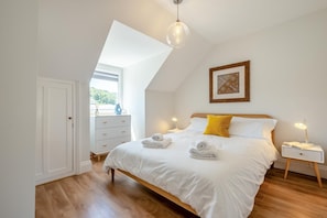 Une chambre à coucher comprenant un lit, des tables de chevet, une commode, une fenêtre et un luminaire au plafond.