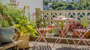 A terrace with potted plants, a table with a bowl and book, and a view of a hillside with buildings. - 1 Bed in Looe (oc-s29019) (Looe)