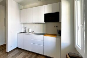 A compact kitchen with white cabinetry, a black microwave, and a wooden countertop. - Alma Suites - Terrace Penthouse (Firenze)