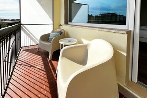 Ein Balkon mit zwei weißen Stühlen und einem kleinen Tisch, ein Fenster mit Blick auf Gebäude und ein gefliester Boden.