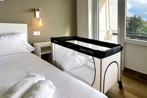 A hotel room with a bed, a bedside table, a lamp, and a window with a view of buildings and trees. - Alma Suites - Terrace Penthouse (Firenze)