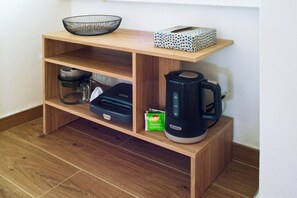 Ein Holzregal mit Kaffeemaschine, Wasserkocher, einem Glasbehälter und einer deckenmusterigen Kiste.