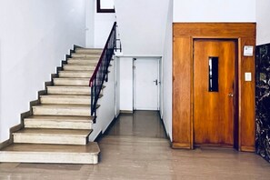 A staircase with beige steps leading to a white door, a wooden door with a small window, and a marble wall. - Alma Suites - Terrace Penthouse (Firenze)