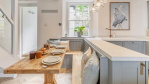 Uma cozinha moderna com uma mesa de jantar de madeira posta para o café da manhã, uma janela com vista para o verde e um quadro de pássaros na parede.
