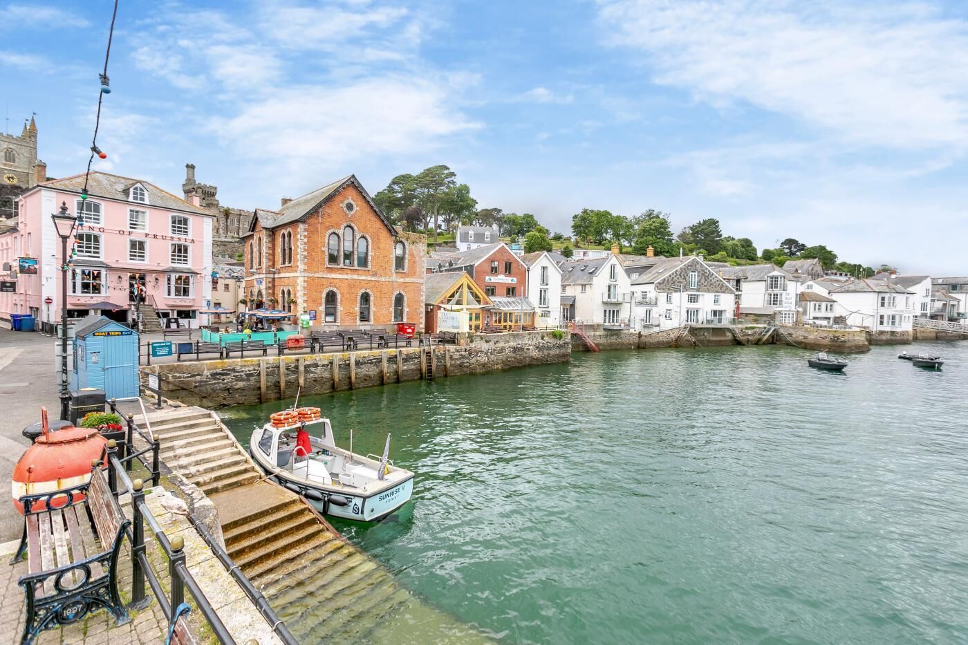 A waterfront scene with a historic building labeled "King of Prussia," a dock with a small boat, and a stone pier with benches.
