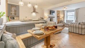 Cozinha moderna com ilha central, sala de jantar com mesa de madeira e sala de estar com sofás listrados.