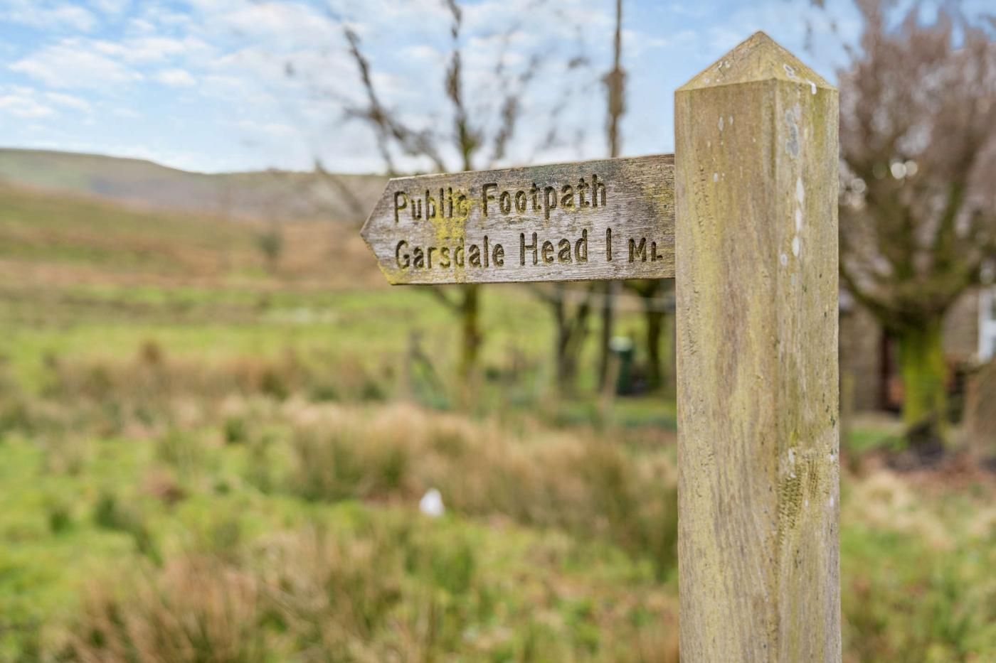 Un panneau indicateur en bois, surmonté d’une flèche pointant vers la gauche, indique un sentier public et la direction de Garsdale Head.