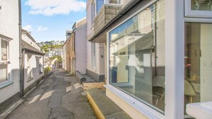 A narrow street with buildings on either side, featuring large windows and a clear sky. - 2 Bed in Polruan (oc-denzil) (Fowey)