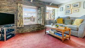A living room with a stone wall, a television, a sofa, and a coffee table. - 2 Bed in Polruan (oc-denzil) (Fowey)