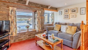 A living room with a stone wall, a television, a sofa, and a coffee table. - 2 Bed in Polruan (oc-denzil) (Fowey)
