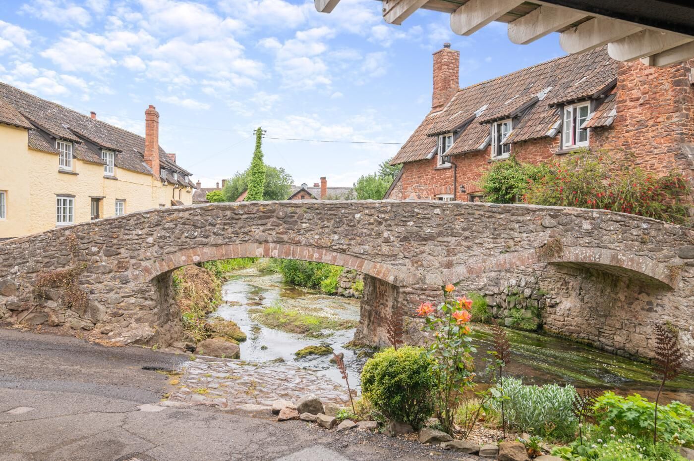 A stone bridge over a narrow stream, surrounded by traditional stone buildings with pitched roofs.