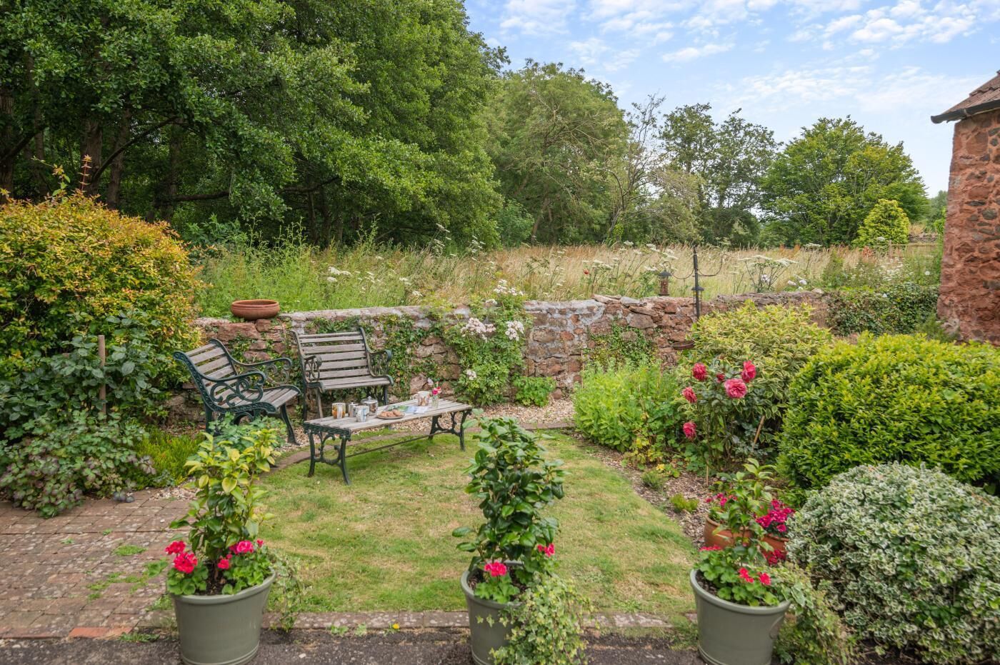 Un jardin avec un mur en pierre, un banc en bois et des plantes en pot.
