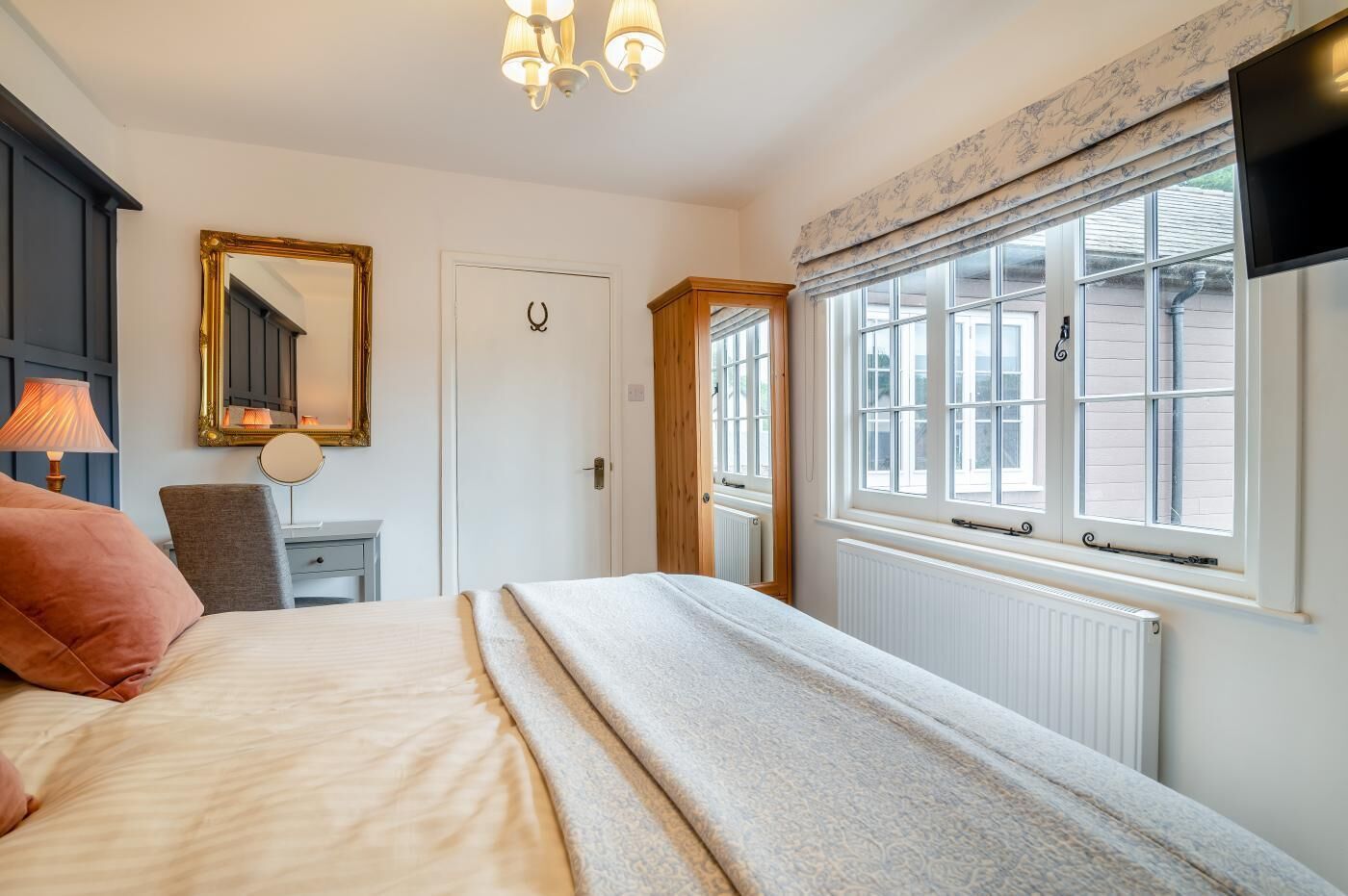 A bedroom with a bed, a desk, a chair, a mirror, a window, and a television.