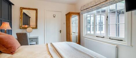 A bedroom with a bed, a desk, a chair, a mirror, a window, and a television.