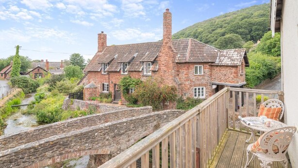 A stone bridge over a stream, a wooden deck with chairs, and a brick house with a chimney. - 2 Bed in Allerford (oc-r29129) (Allerford)