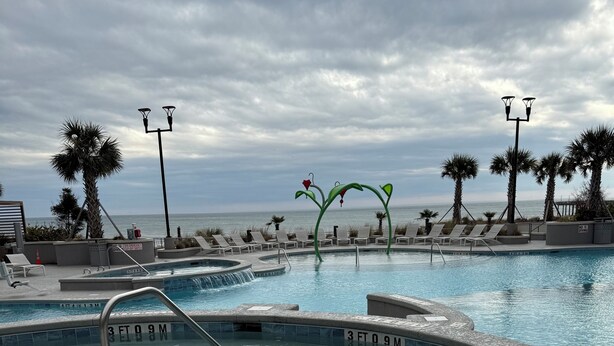 A pool area with multiple hot tubs and lounge chairs, a clear view of the ocean, and a cloudy sky. - Best, New, Luxurious Oceanfront Resort- Myrtle Beach, SC- 2 Bedroom, 2 Bathroom (Myrtle Beach)
