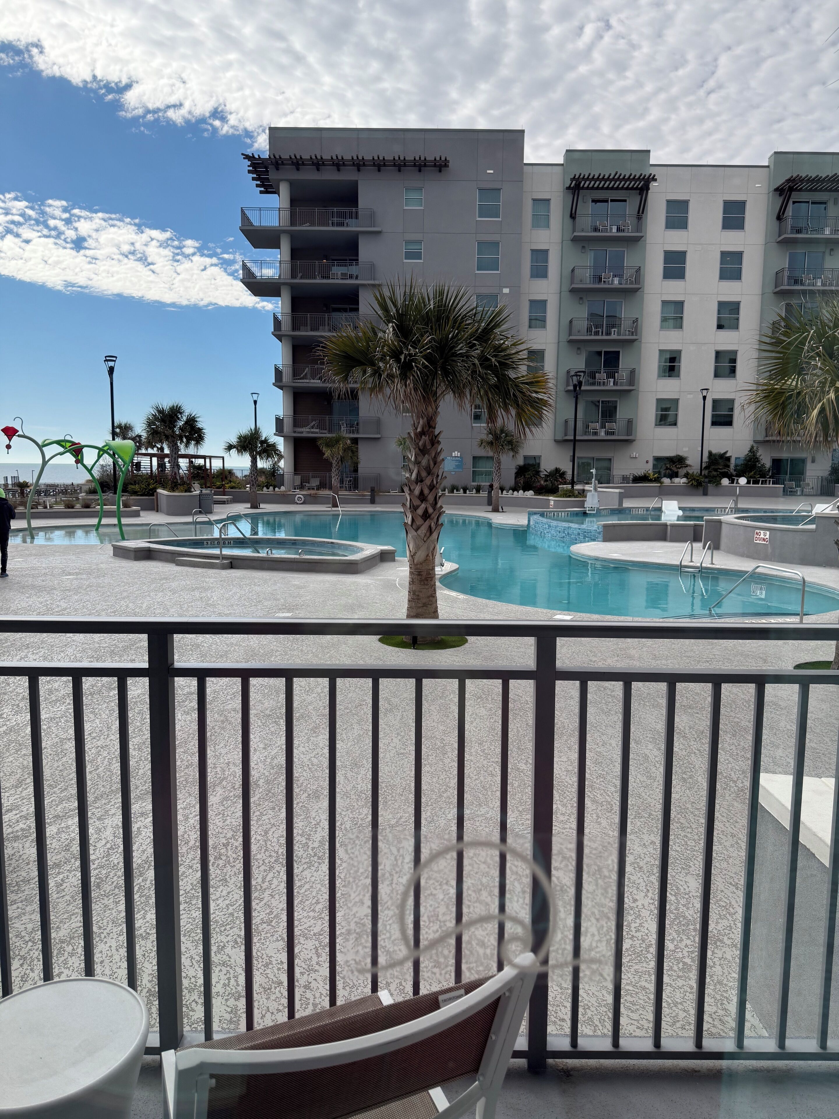 A pool area with a palm tree, a chair, and a building with balconies in the background.
