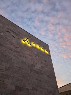 Un edificio con fachada de ladrillo y letras iluminadas que deletrean 'BARKA' contra un cielo crepuscular.