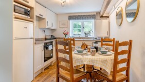 A compact kitchen with white cabinets, a built-in oven, and a dining table set for four with wooden chairs. - 1 Bed in Allerford (oc-m29128) (Allerford)