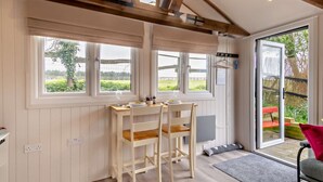 Ein gemütliches Zimmer mit einem Holztisch und -stühlen, großen Fenstern und Blick ins Freie.