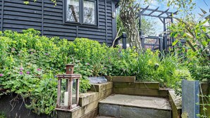 Ein Garten mit einer Holzbank, einem Laternen und einem Haus im Hintergrund.