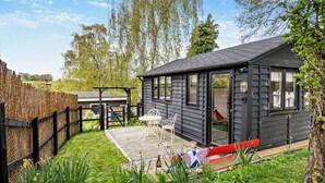 Eine kleine Holzhütte mit Terrasse, einem eingezäunten Garten und einer roten Bank.