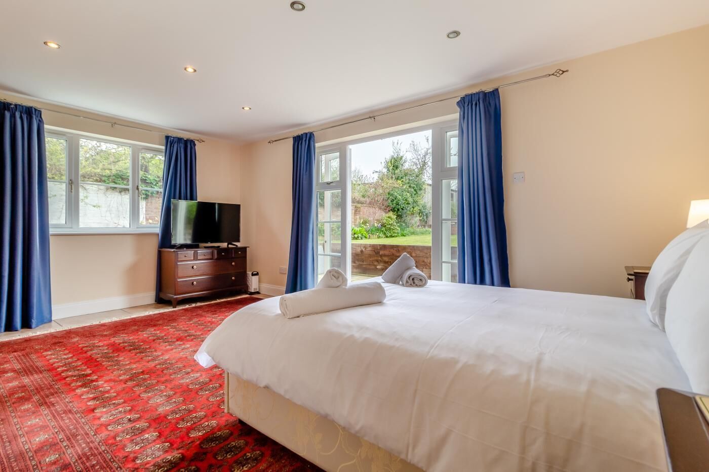 A hotel room with a large bed, a TV, and a view of the garden through the windows.